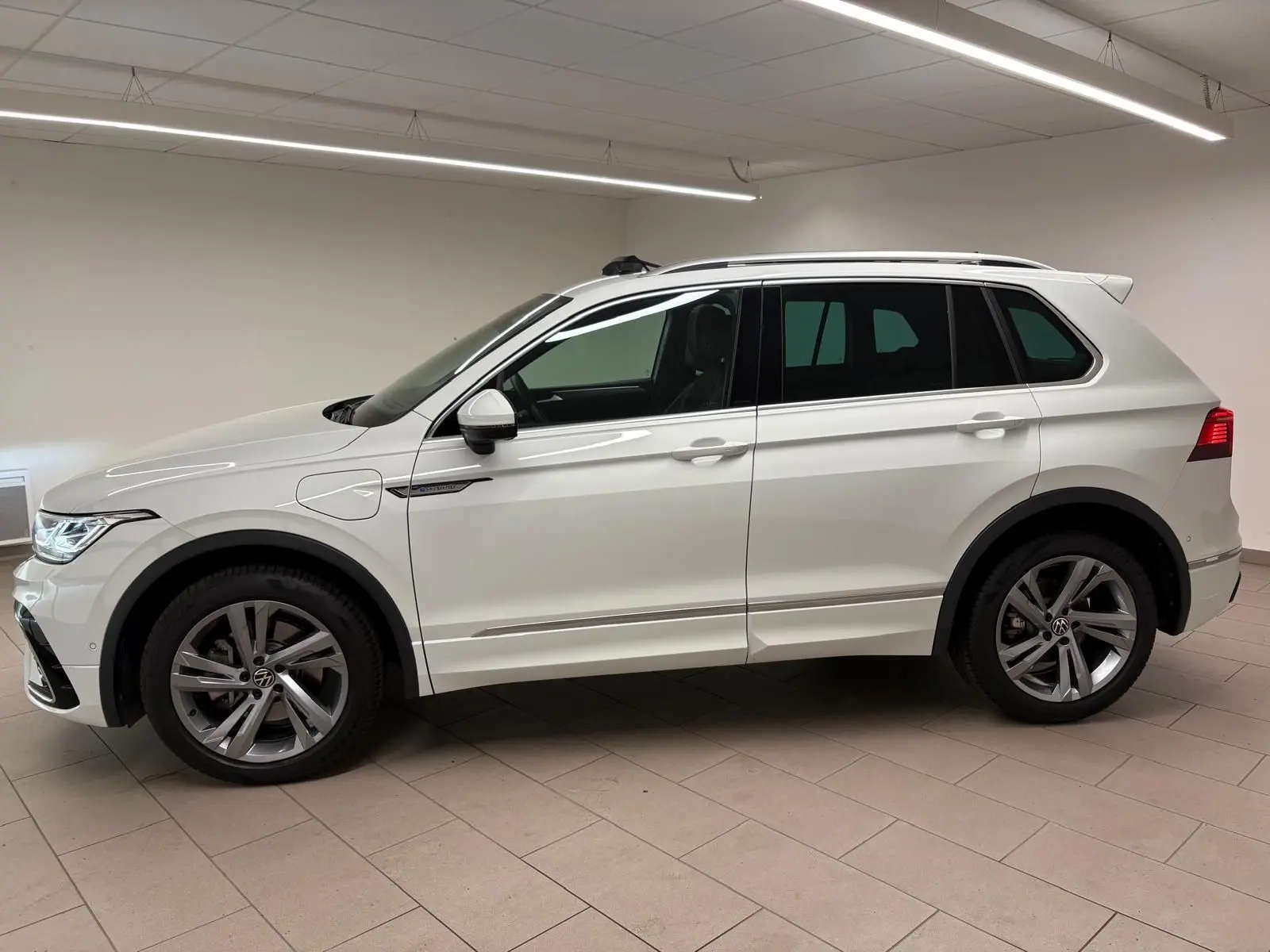 Profil droit d'un Volkswagen Tiguan blanc pur 2023 hybride rechargeable avec jantes R-Line distinctives en intérieur neutre.