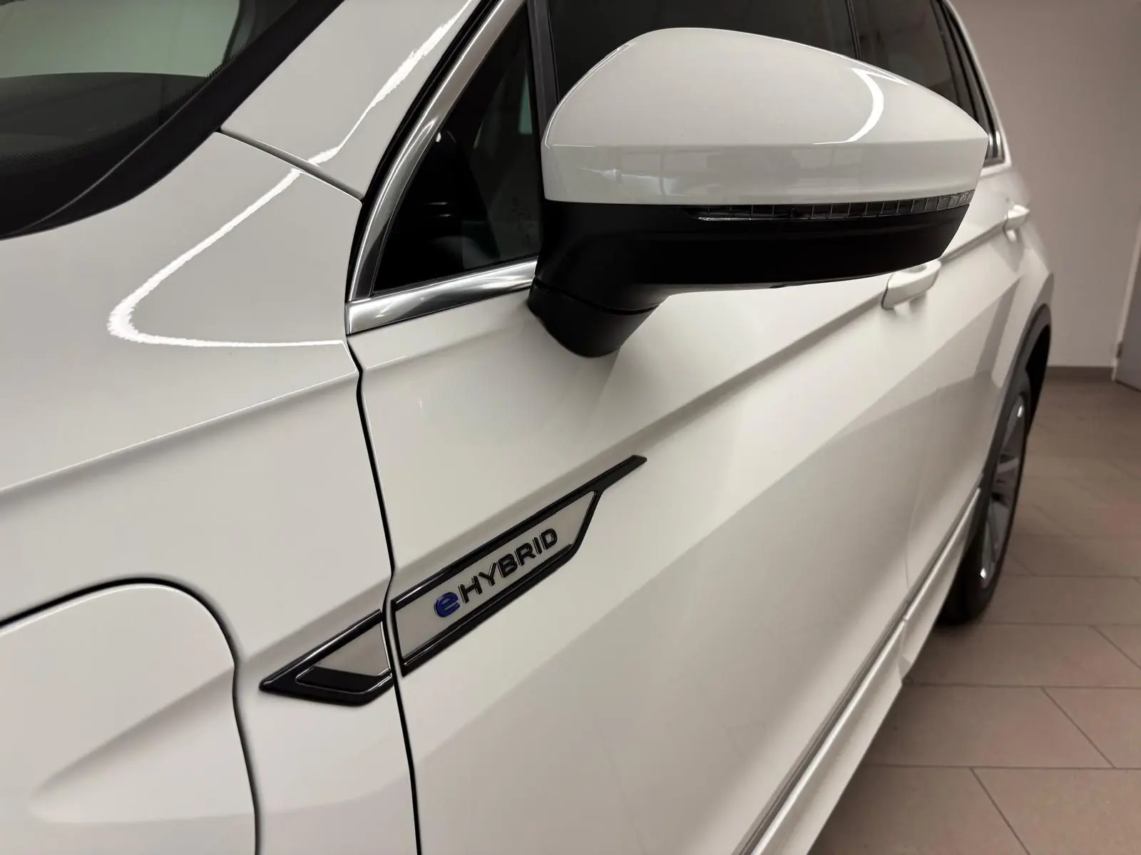 Gros plan sur le côté gauche blanc pur du Volkswagen Tiguan 1.4 eHybrid 2023 avec logo eHybrid et rétroviseur.