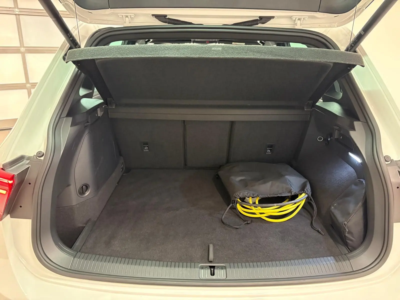 Coffre ouvert d'un Volkswagen Tiguan blanc pur 2023, version hybride rechargeable, avec câble de recharge visible.