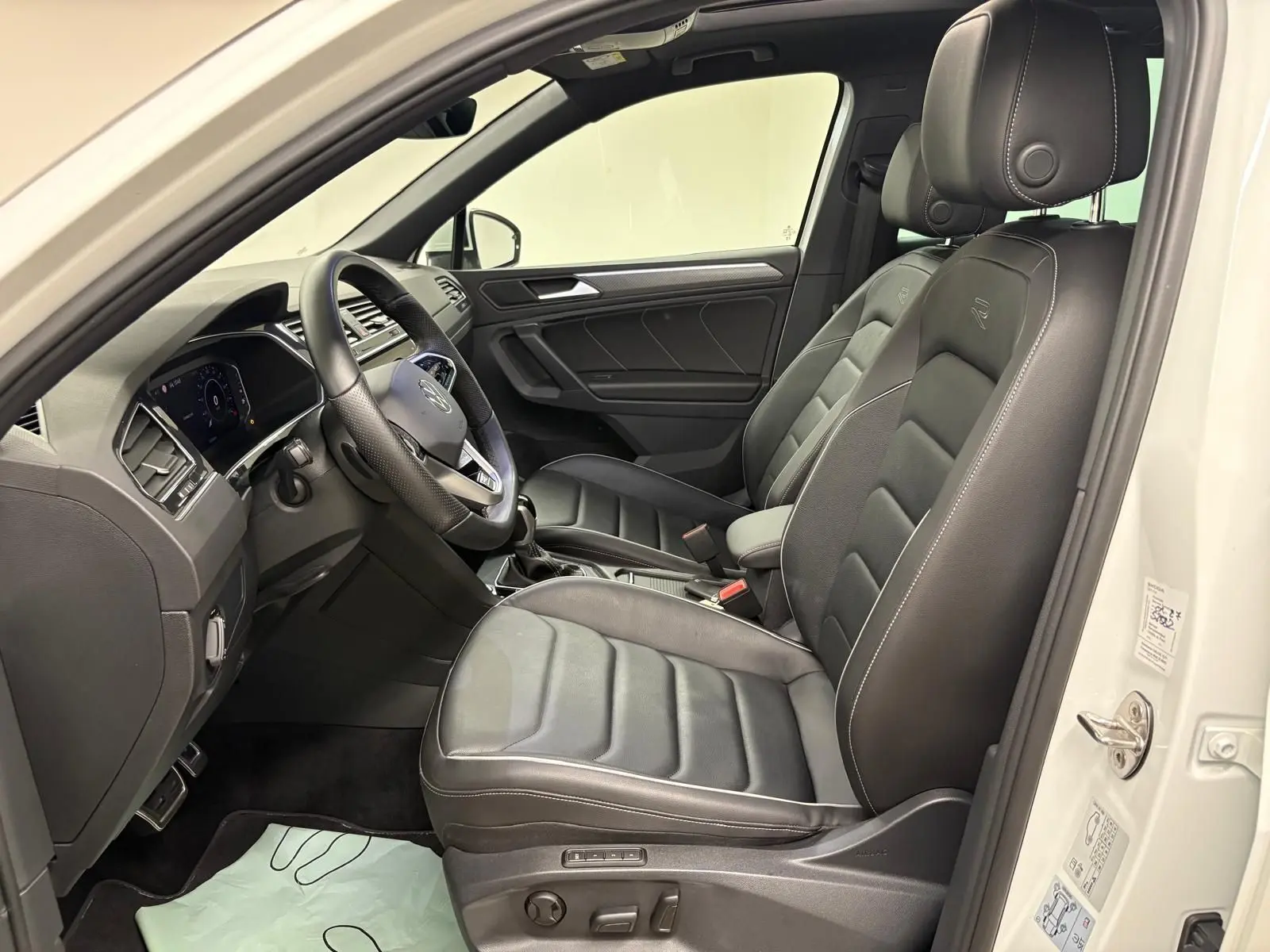Vue intérieure côté conducteur du Volkswagen Tiguan blanc pur 2023, sièges en cuir noir R-Line exclusifs.