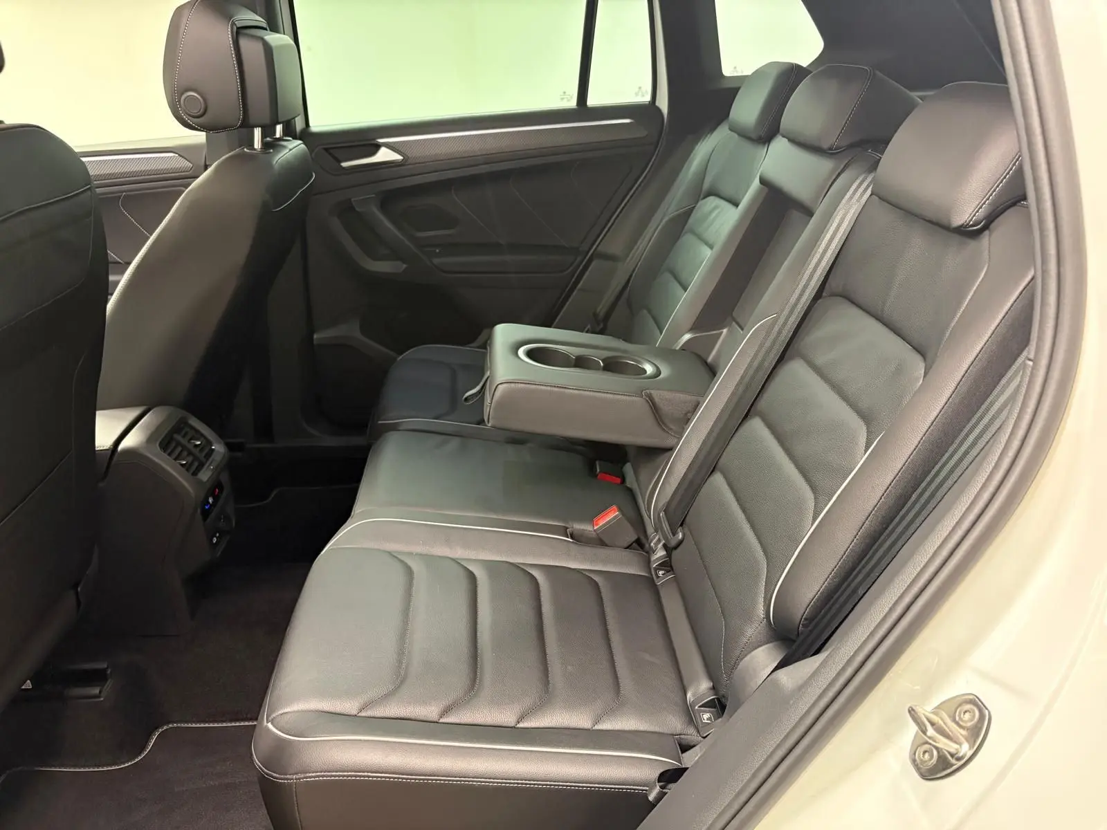 Vue intérieure côté droit des sièges arrière noirs en cuir du Volkswagen Tiguan blanc pur 2023, avec accoudoir central relevé.