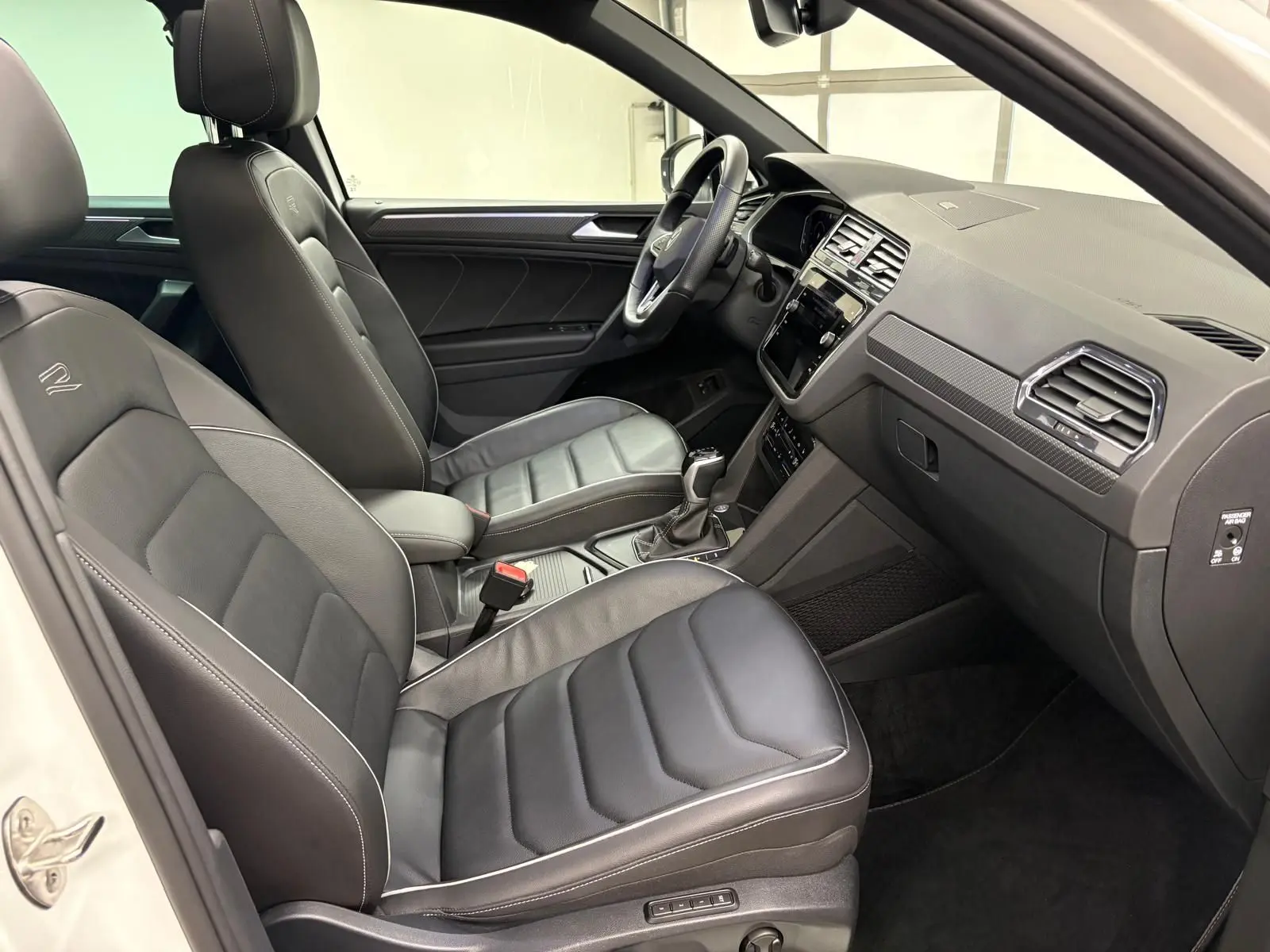 Intérieur noir du Volkswagen Tiguan 2023 vu côté passager, avec sièges en cuir R-Line et tableau de bord moderne.