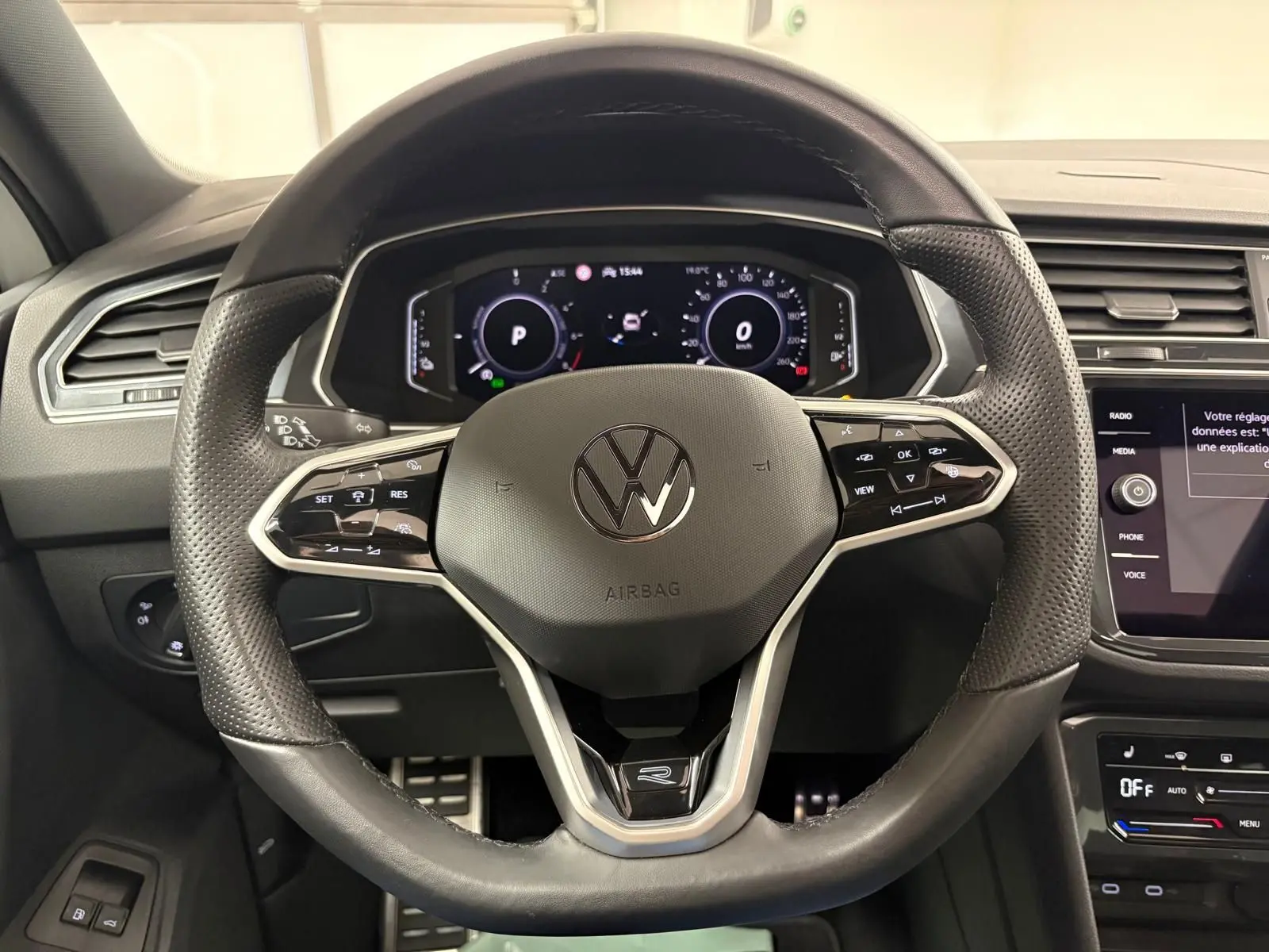 Vue rapprochée du volant noir perforé du Volkswagen Tiguan 1.4 eHybrid 2023 avec tableau de bord numérique allumé.