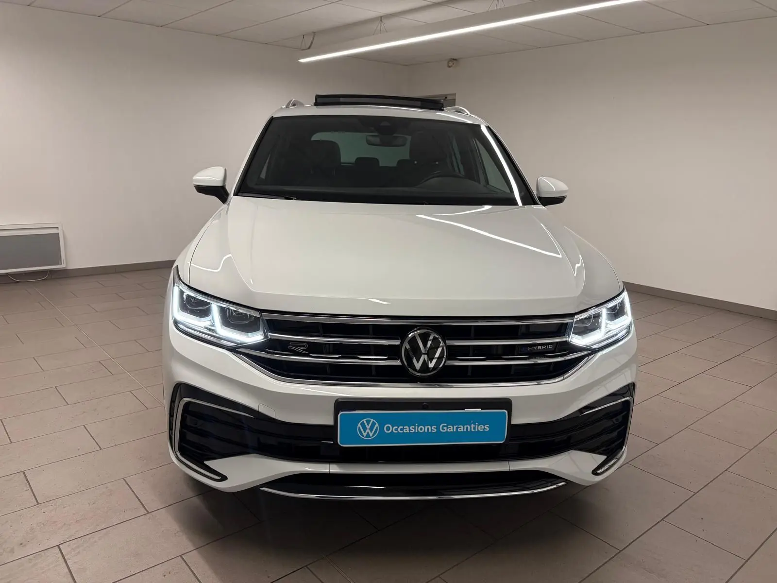 Vue frontale d'un Volkswagen Tiguan blanc pur 2023, version hybride rechargeable R-Line Exclusive avec phares LED allumés.