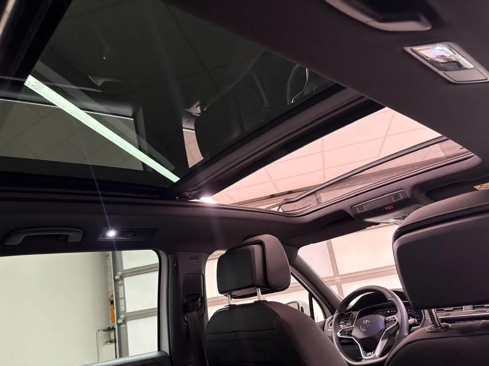 Toit panoramique ouvert et intérieur noir du Volkswagen Tiguan 1.4 eHybrid 2023 vu depuis l'arrière côté gauche.