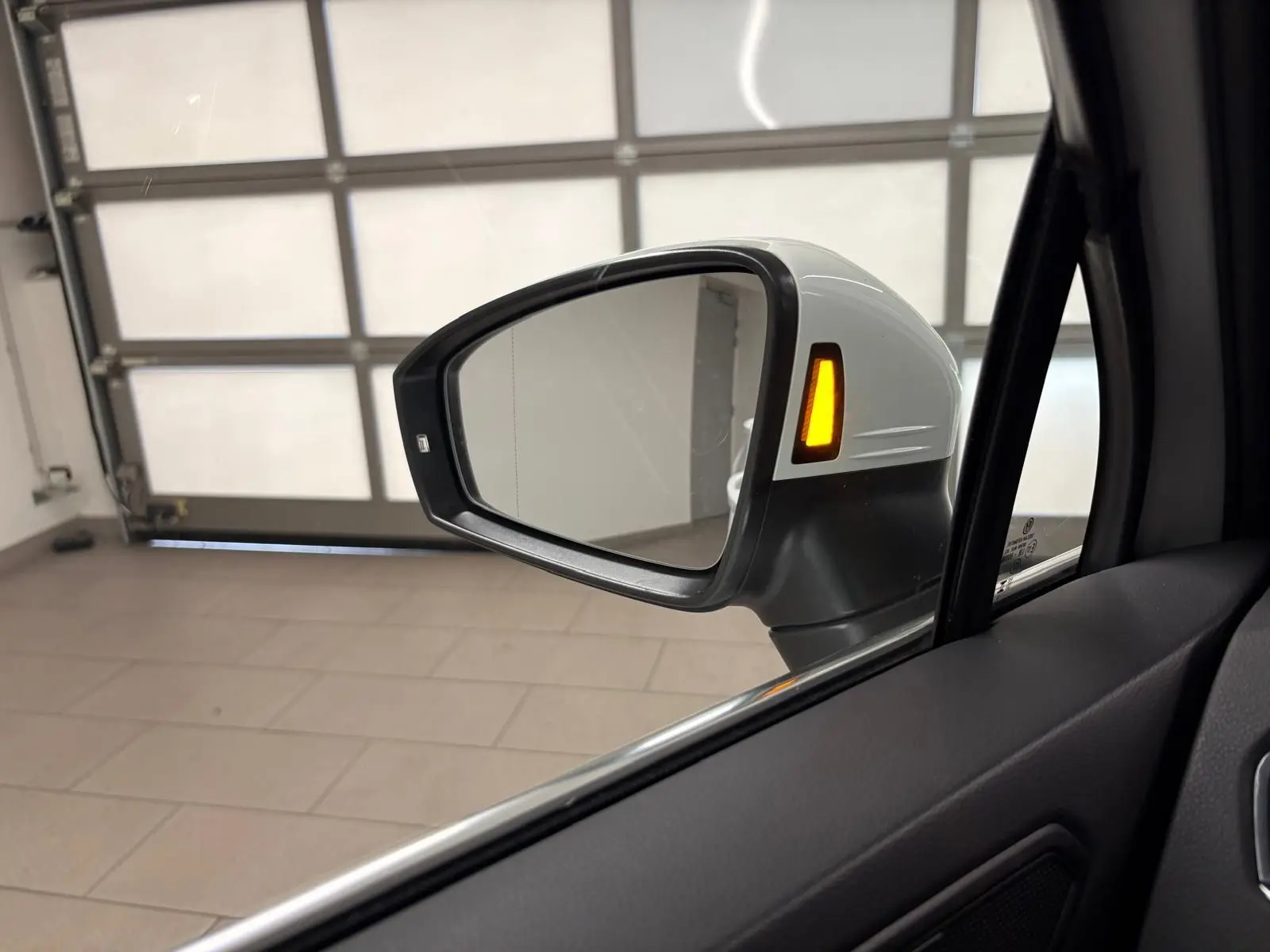 Rétroviseur extérieur côté gauche blanc pur du Volkswagen Tiguan 1.4 eHybrid 2023 avec clignotant allumé en intérieur de garage.