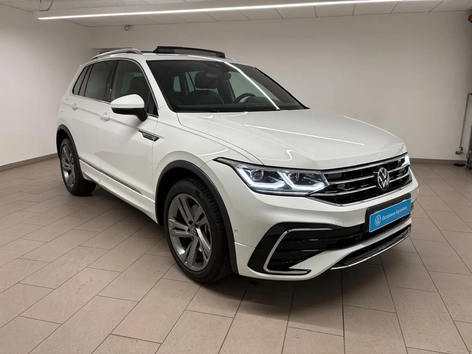 Volkswagen Tiguan 1.4 eHybrid blanc pur en vue 3/4 avant droit, avec finition R-Line Exclusive et phares LED allumés.