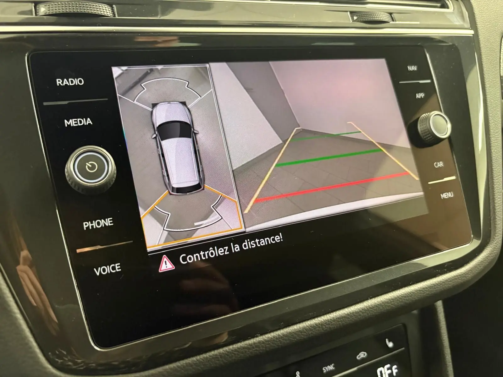 Écran multimédia du Volkswagen Tiguan 2023 blanc pur montrant la caméra de recul avec vue aérienne et lignes de guidage.