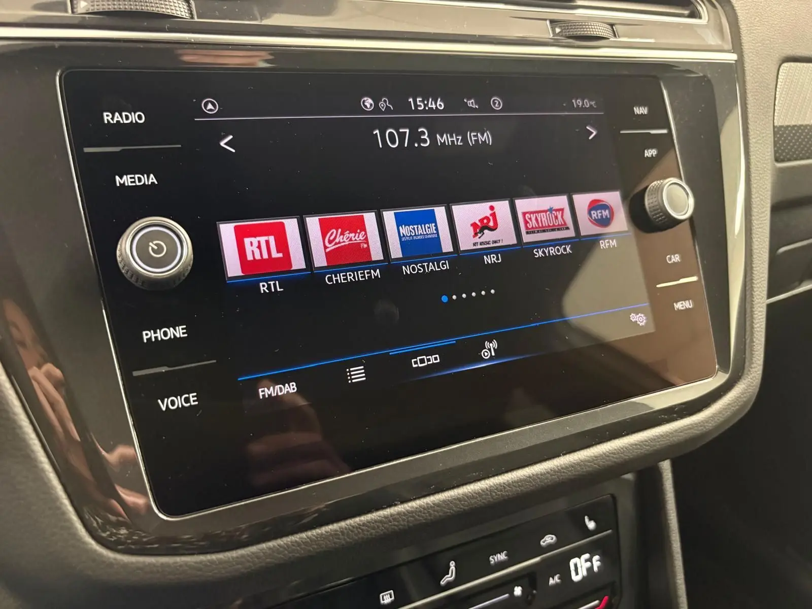 Écran tactile central du Volkswagen Tiguan 2023 blanc, affichant les stations radio FM avec commandes autour.