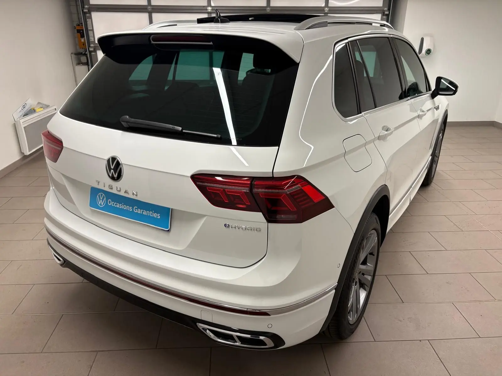 Vue 3/4 arrière droite d'un Volkswagen Tiguan blanc pur hybride rechargeable avec finition R-Line Exclusive et feux LED distinctifs.