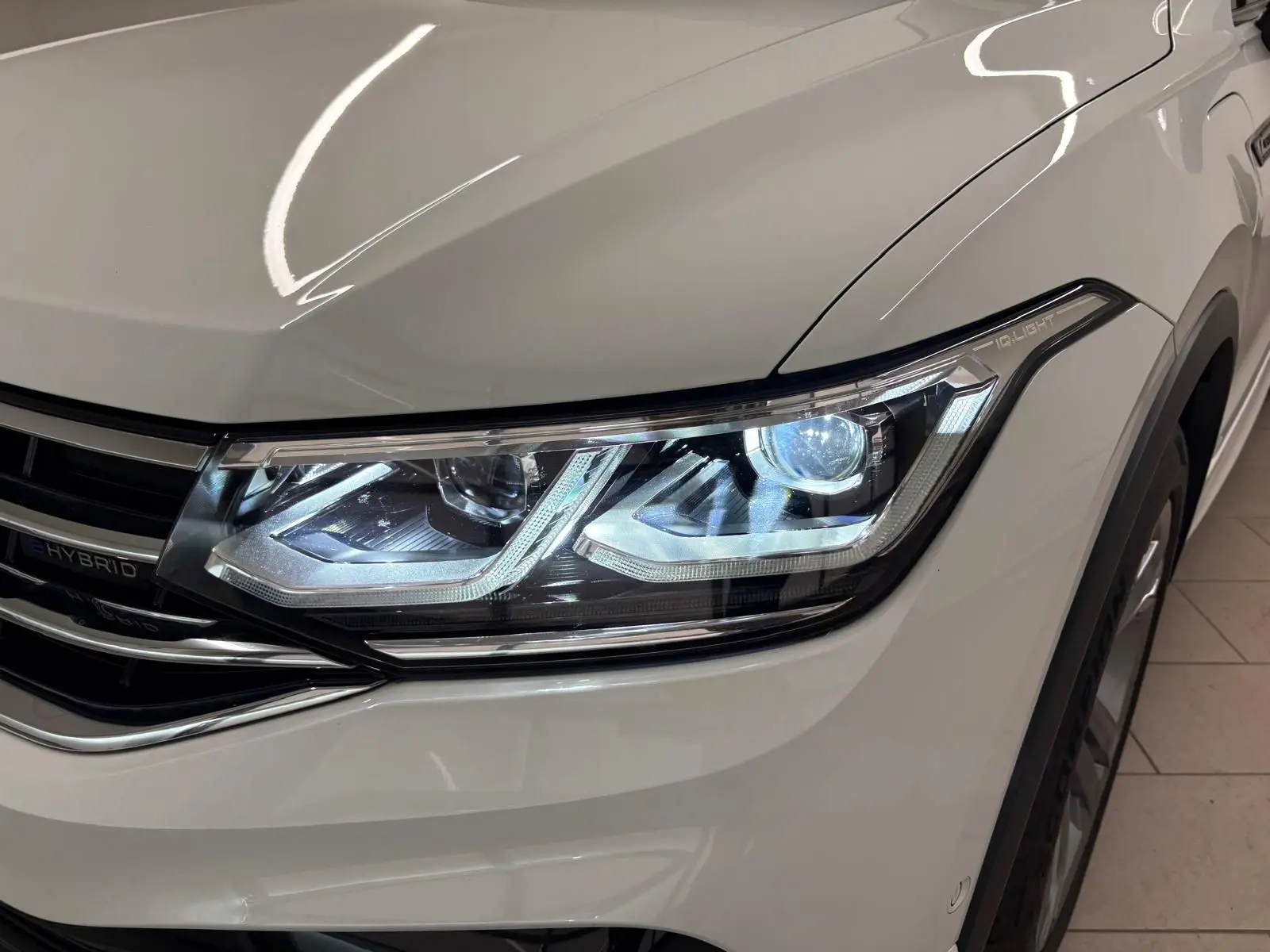 Gros plan sur le phare avant droit allumé du Volkswagen Tiguan blanc pur 1.4 eHybrid R-Line Exclusive 2023.