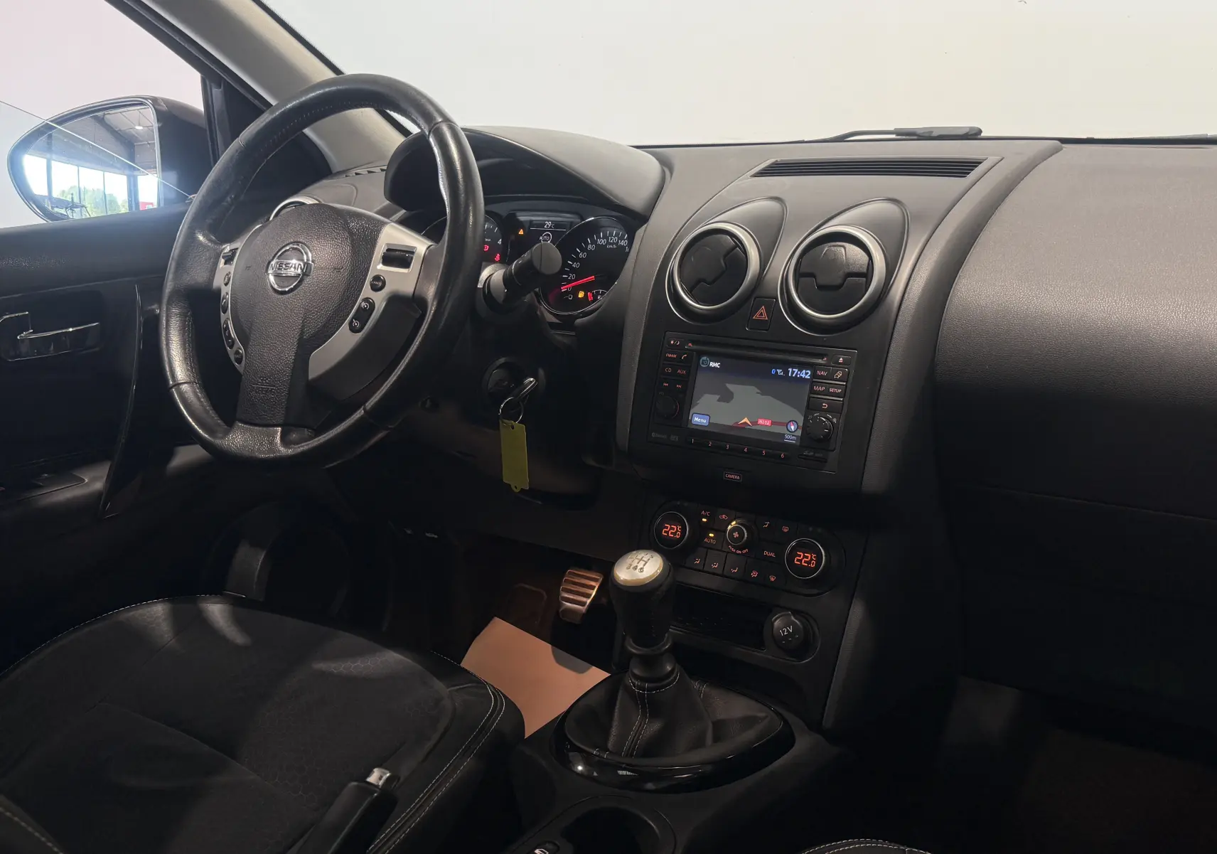 Intérieur du Nissan Qashqai+2 2014 en vue du poste de conduite, volant, tableau de bord et levier de vitesses manuelle visibles.