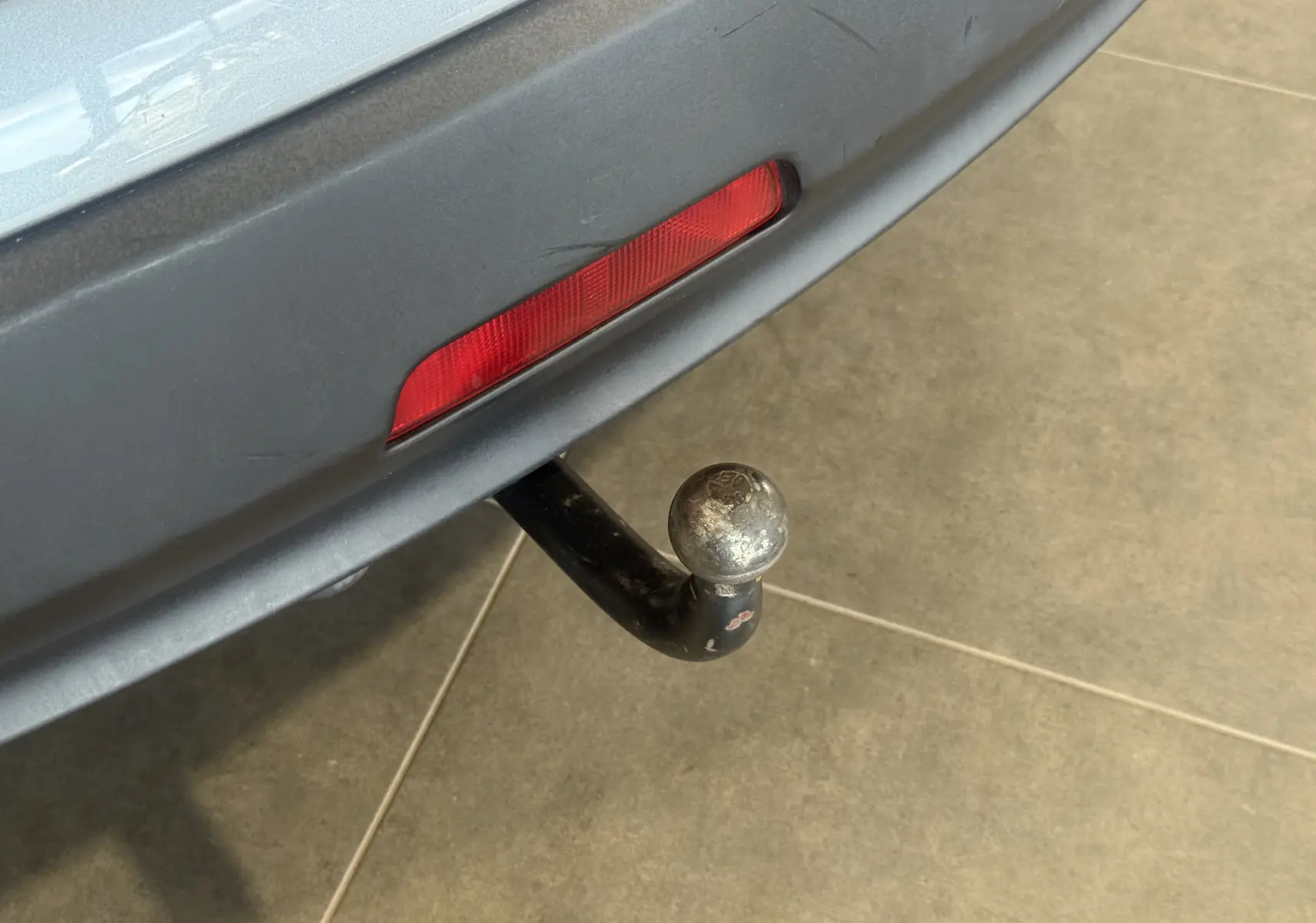 Gros plan sur l'attelage de remorque sous le pare-chocs arrière gris d'un Nissan Qashqai+2 Tekna 2014.