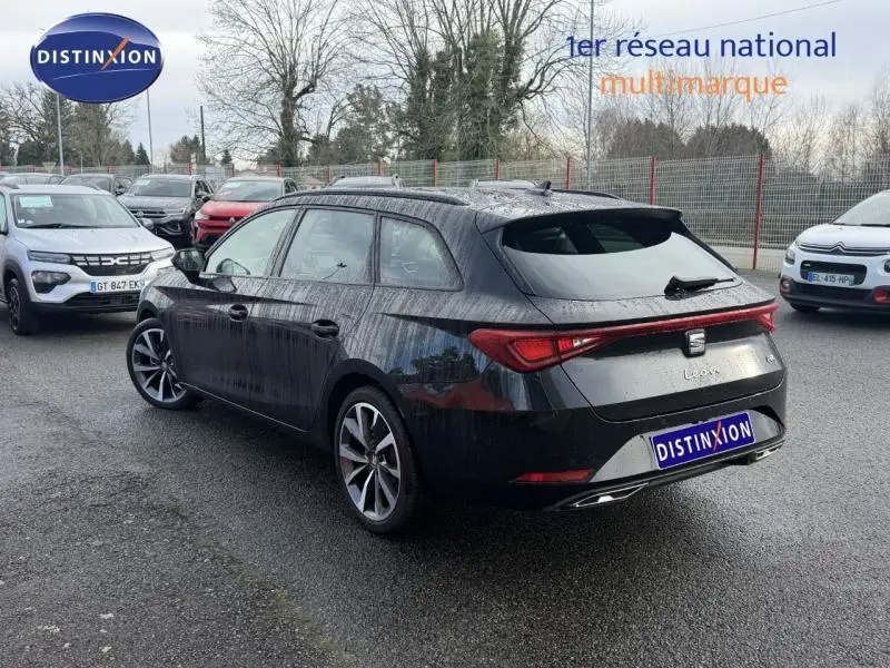Vue 3/4 arrière droite d'une SEAT LEON ST 1.5 eTSI Hybrid noire métallisée avec feux arrière reliés et jantes alliage.