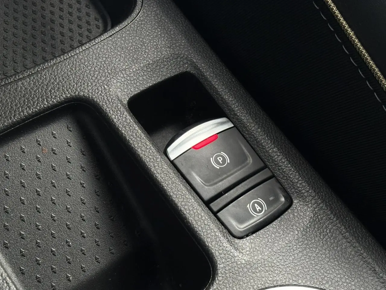 Gros plan sur la console centrale noire de la Renault Symbioz, avec les boutons du frein de parking électrique et de l'auto-hold.