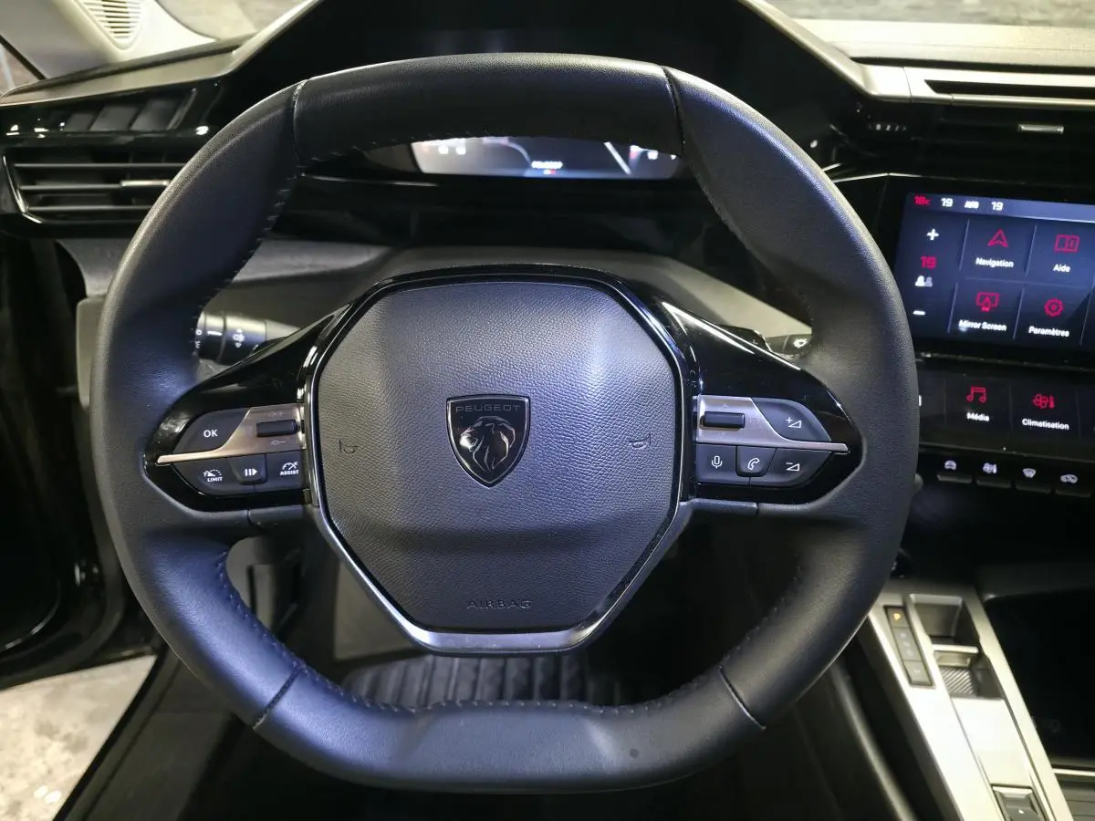 Vue rapprochée du volant noir cuir de la Peugeot 308 SW 2024 avec commandes intégrées et écran tactile à droite.