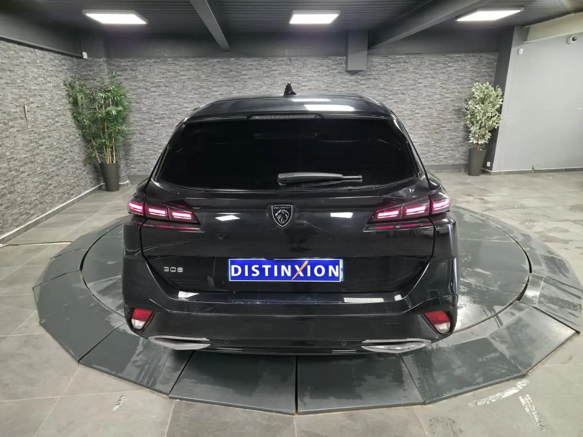 Vue arrière d'une Peugeot 308 SW noire 2024 avec feux LED allumés et logo lion distinctif au centre.