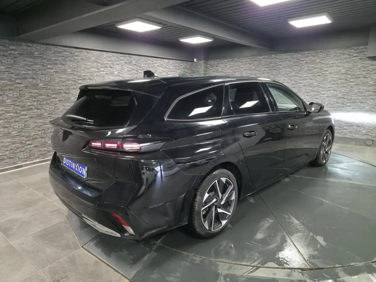 Peugeot 308 SW noire vue en 3/4 arrière droit dans un showroom avec jantes alliage et vitres surteintées.
