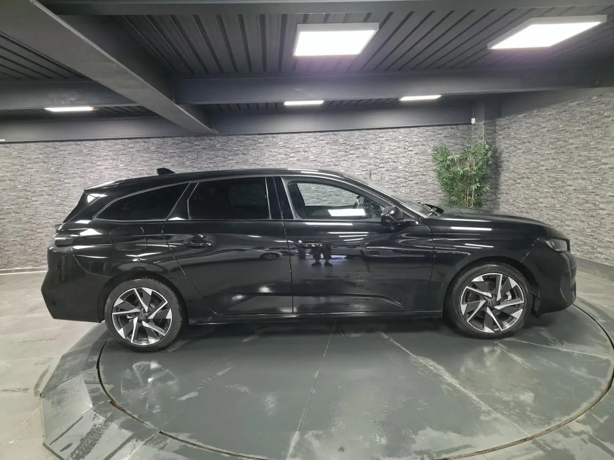 Peugeot 308 SW noire vue de profil côté gauche, avec jantes alliage 17'' et vitres surteintées en intérieur showroom.