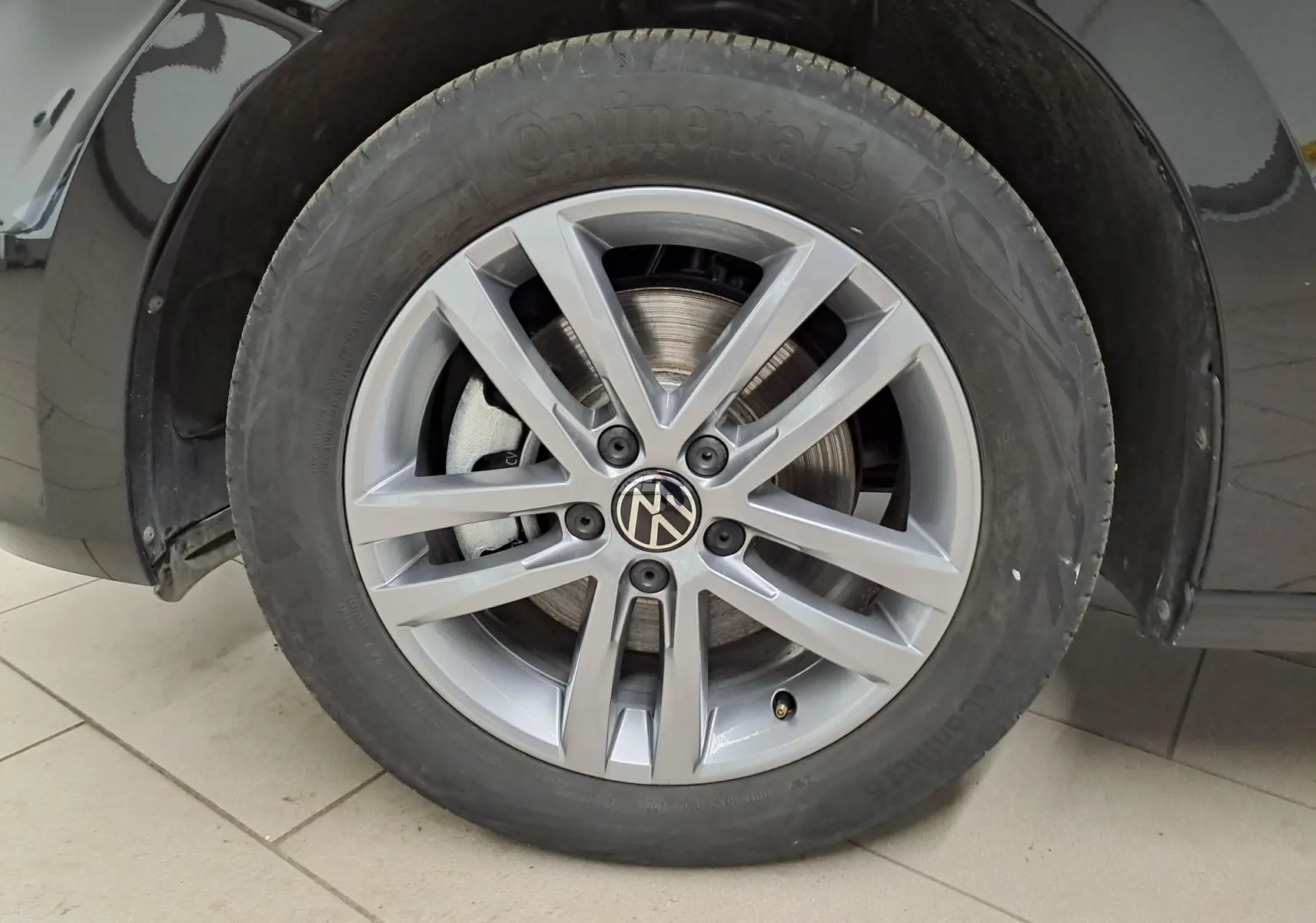 Gros plan sur la roue avant gauche du Volkswagen Touran 2025 noir intense nacré, jante alliage à 5 doubles branches.