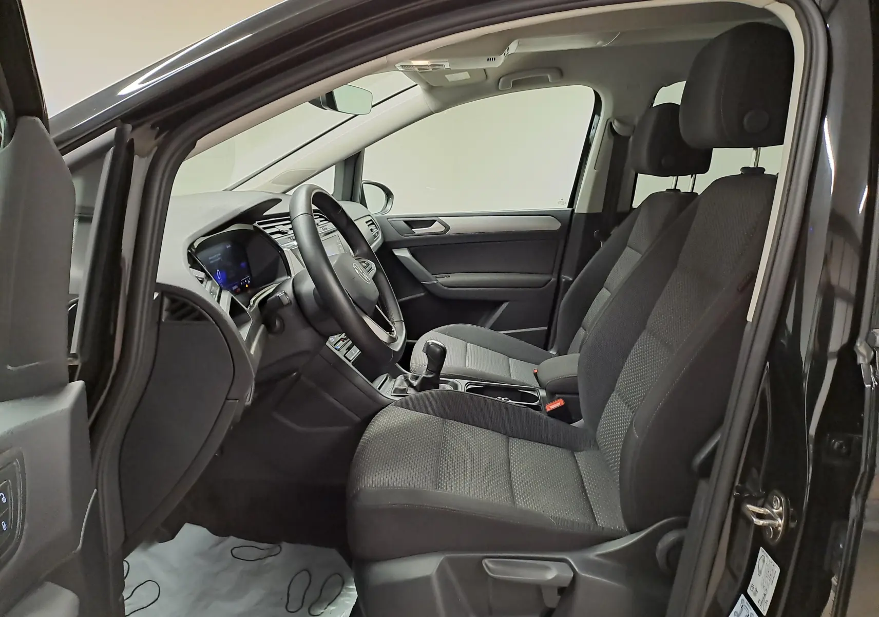 Intérieur avant droit du Volkswagen Touran 2025 noir intense nacré, sièges tissu gris et tableau de bord moderne.
