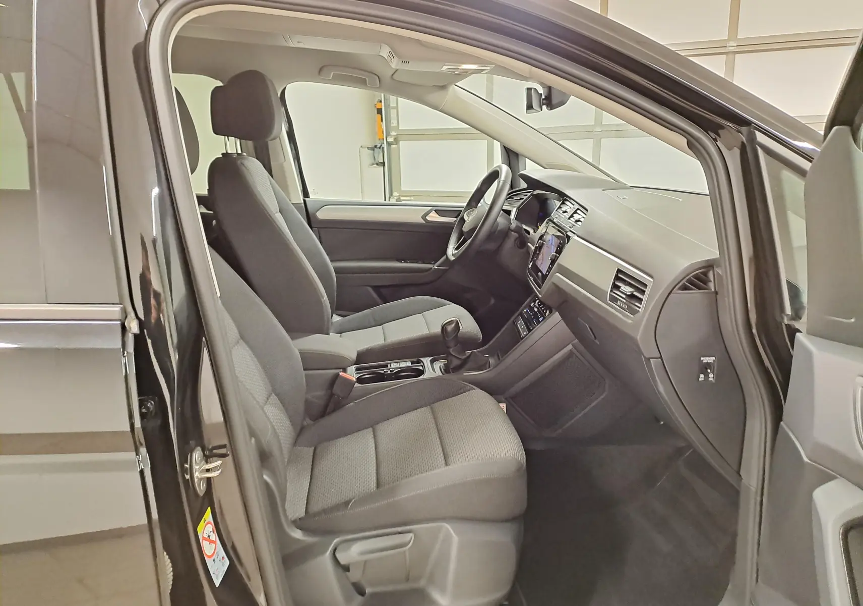 Vue intérieure côté conducteur du Volkswagen Touran noir intense nacré, mettant en valeur les sièges et le tableau de bord moderne.