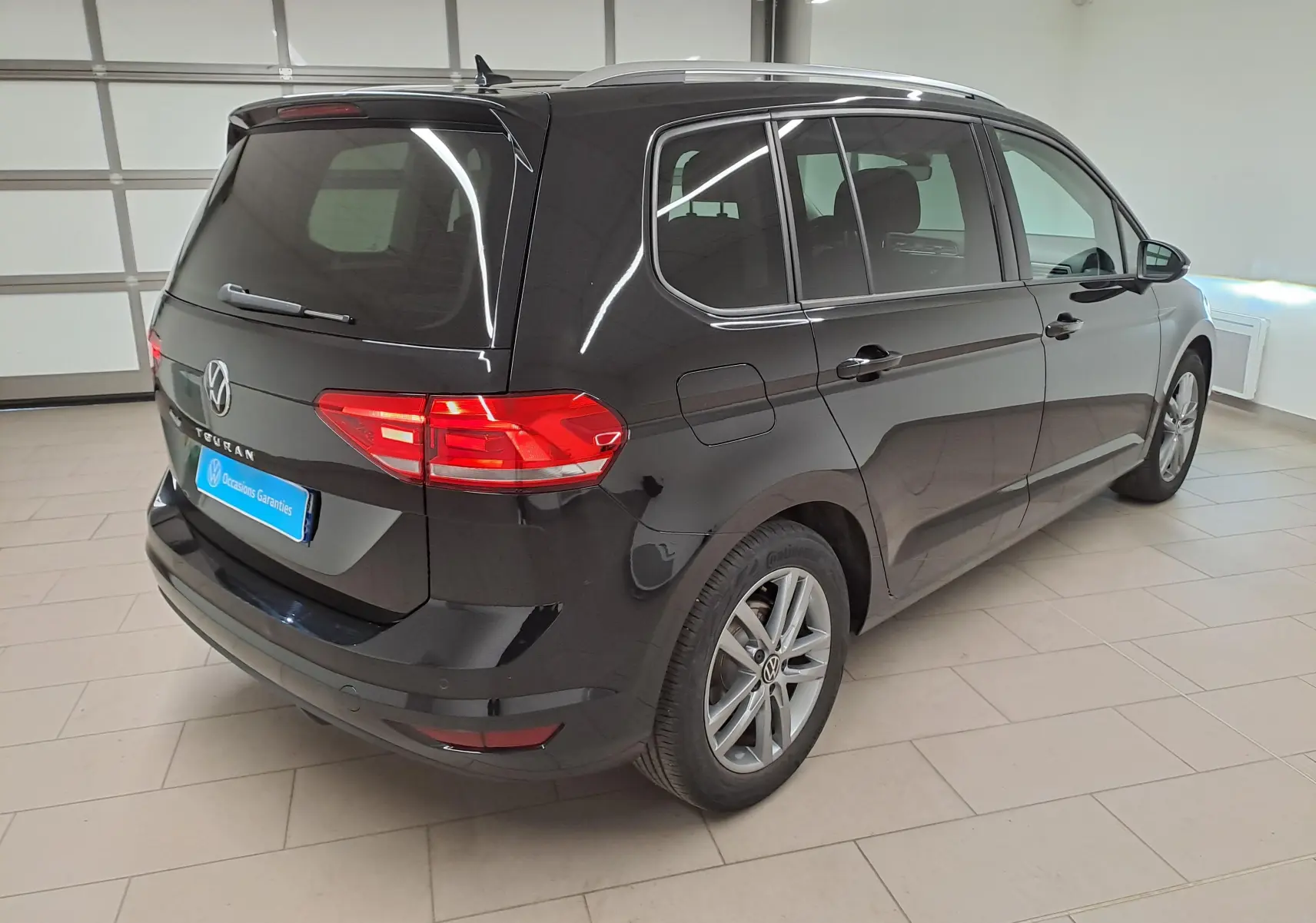 Volkswagen Touran 2025 noir intense nacré vu en 3/4 arrière droit dans un intérieur lumineux.