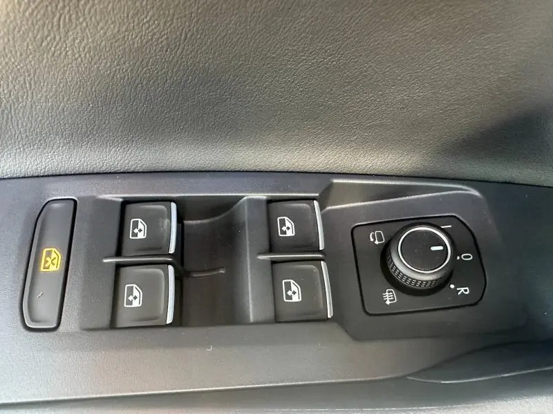 Gros plan sur les commandes de lève-vitres et réglage des rétroviseurs côté conducteur du Volkswagen T-Cross 2025 en Reflet d'Argent.