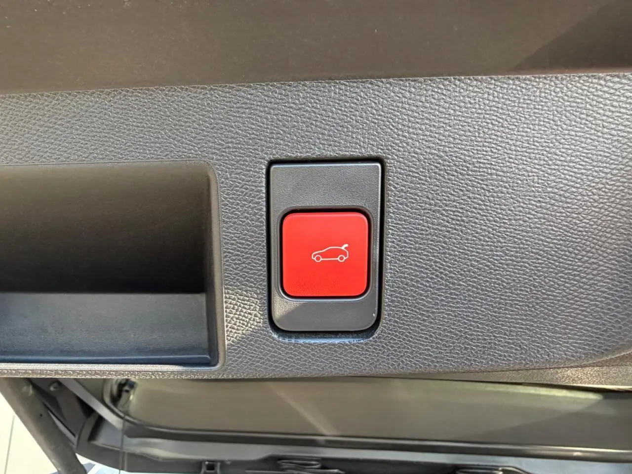 Gros plan sur le bouton rouge d'ouverture électrique du hayon dans le coffre du Citroën C5 Aircross blanc.