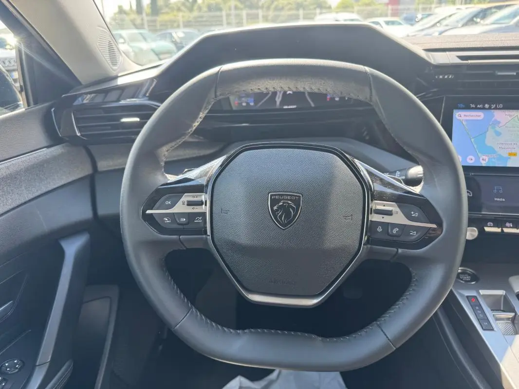 Vue intérieure centrée sur le volant noir de la Peugeot 308 Hybrid 2024 avec tableau de bord numérique et écran tactile.