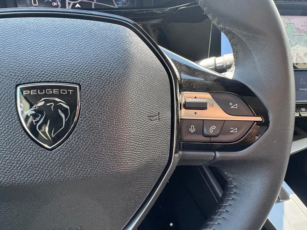 Gros plan sur le volant noir de la Peugeot 308 Hybrid 136 e-DCS6 Allure avec commandes intégrées côté droit.