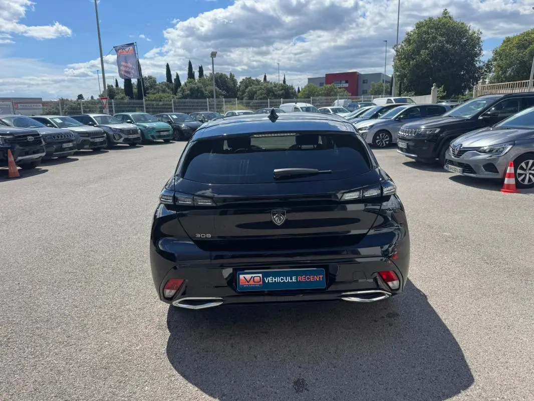 Vue arrière d'une Peugeot 308 Hybrid noire 2024 avec feux LED et double sortie d'échappement chromée sur parking.