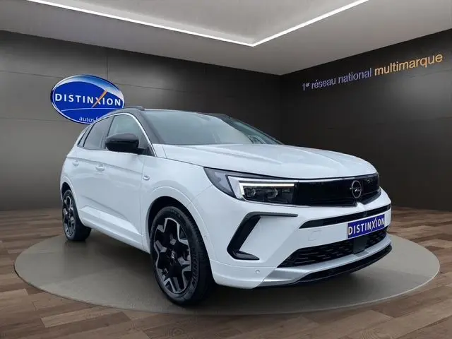 Vue 3/4 avant d'un Opel Grandland blanc Arktis avec toit noir et jantes alliage noires dans un showroom.