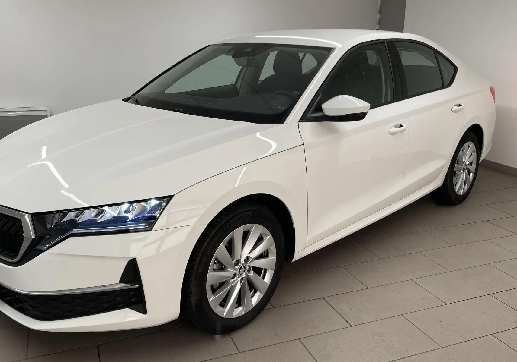 Vue 3/4 avant droite d'une Skoda Octavia 2024 blanc candy avec jantes alliage et phares LED allumés.