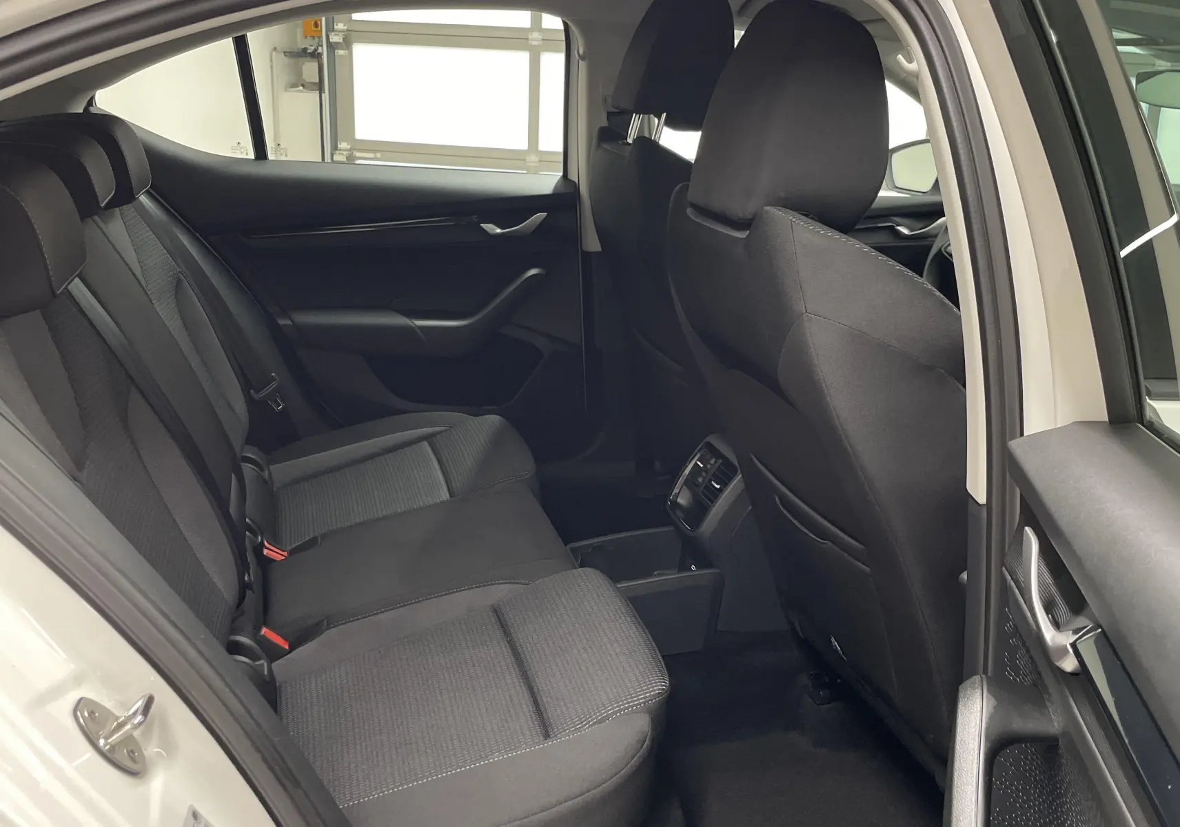 Vue intérieure arrière côté gauche d'une Skoda Octavia blanche 2024 avec sièges tissu noirs et console centrale ouverte.