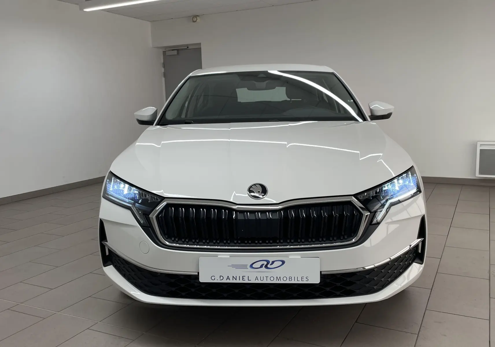 Vue frontale d'une Skoda Octavia 2024 blanc candy avec phares allumés et calandre noire brillante.