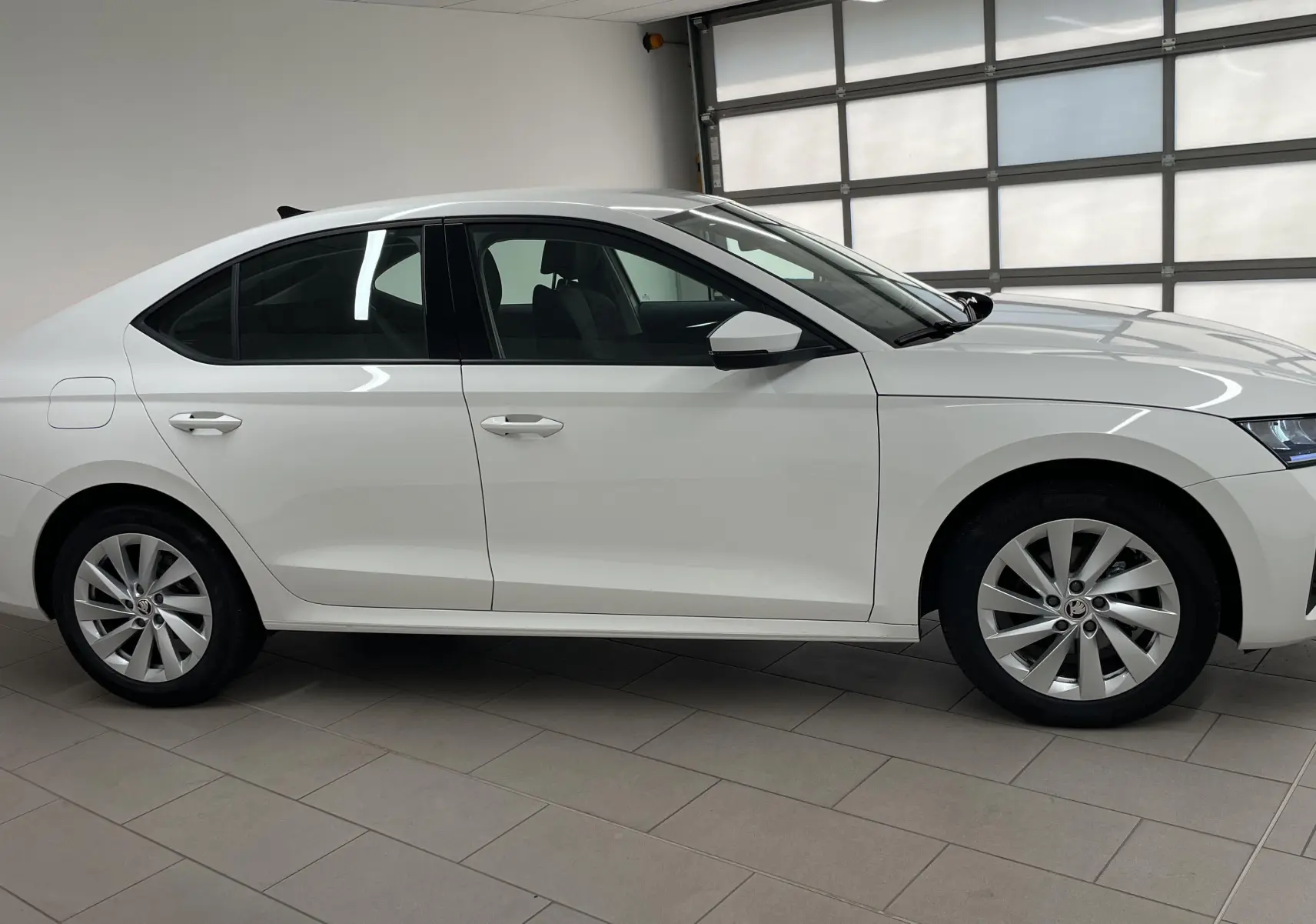 Profil côté gauche d'une Skoda Octavia 2024 blanc candy, berline diesel avec jantes alliage et feux arrière allumés.