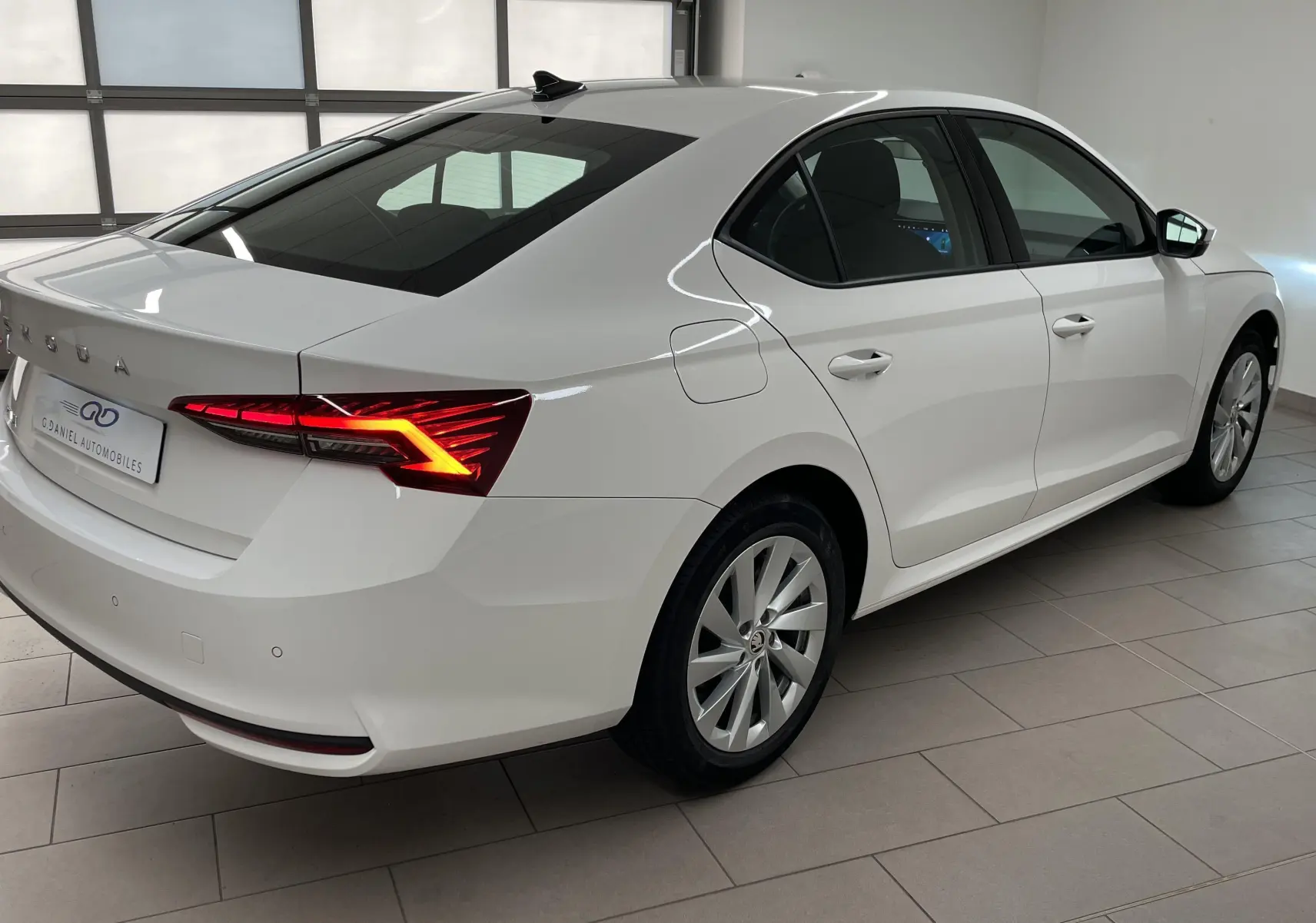 Vue 3/4 arrière droite d'une Skoda Octavia 2024 blanc candy avec feux arrière allumés et jantes alliage.