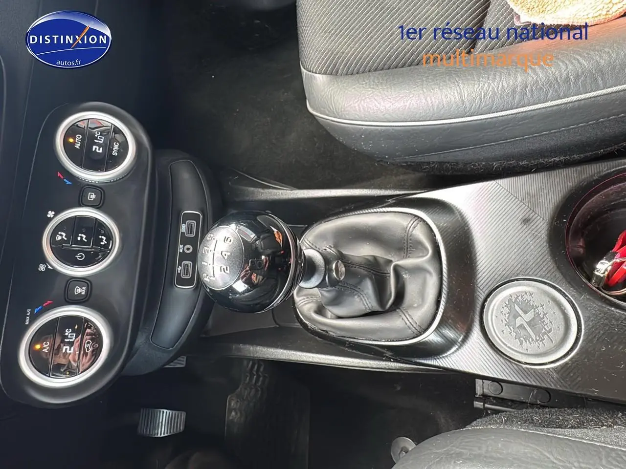 Vue rapprochée de la console centrale de la Fiat 500X rouge, mettant en valeur le levier de vitesse manuel et les commandes de climatisation.