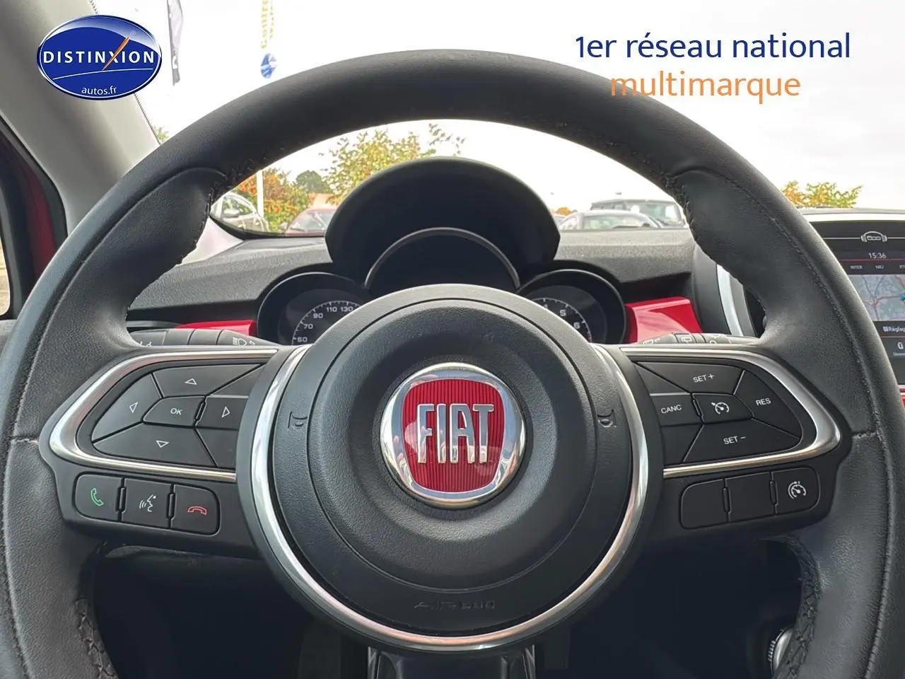 Vue rapprochée du volant cuir multifonction de la FIAT 500X rouge, avec commandes intégrées et tableau de bord visible.