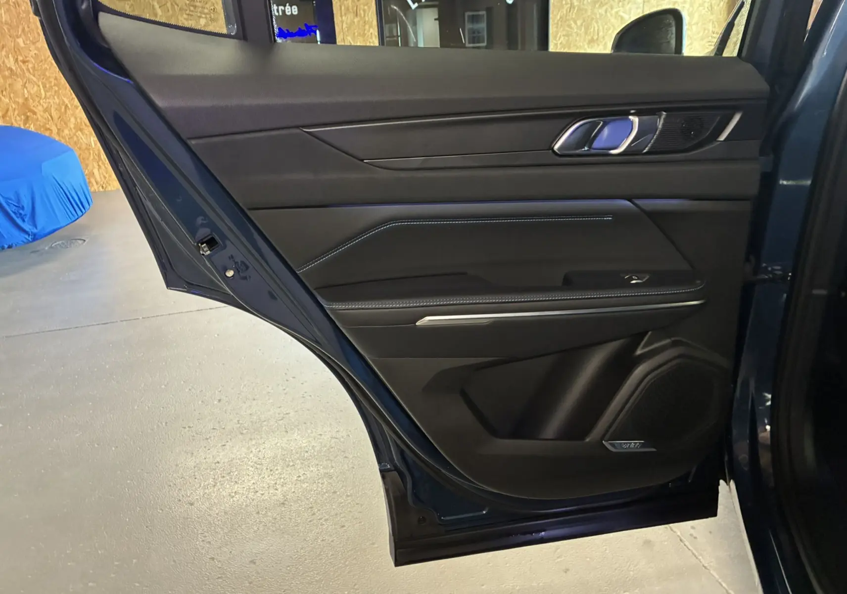 Porte arrière droite ouverte d'un LYNK & CO 01 bleu, intérieur noir avec surpiqûres bleues et haut-parleur signé Bowers & Wilkins.