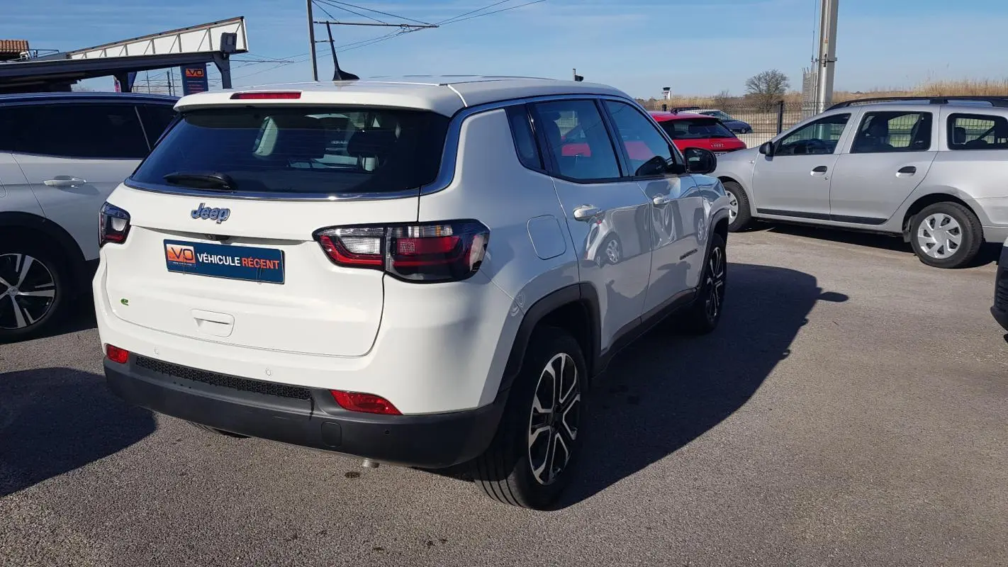 Jeep Compass blanc vu de 3/4 arrière droit, avec jantes alliage 18 pouces et feux arrière LED visibles.