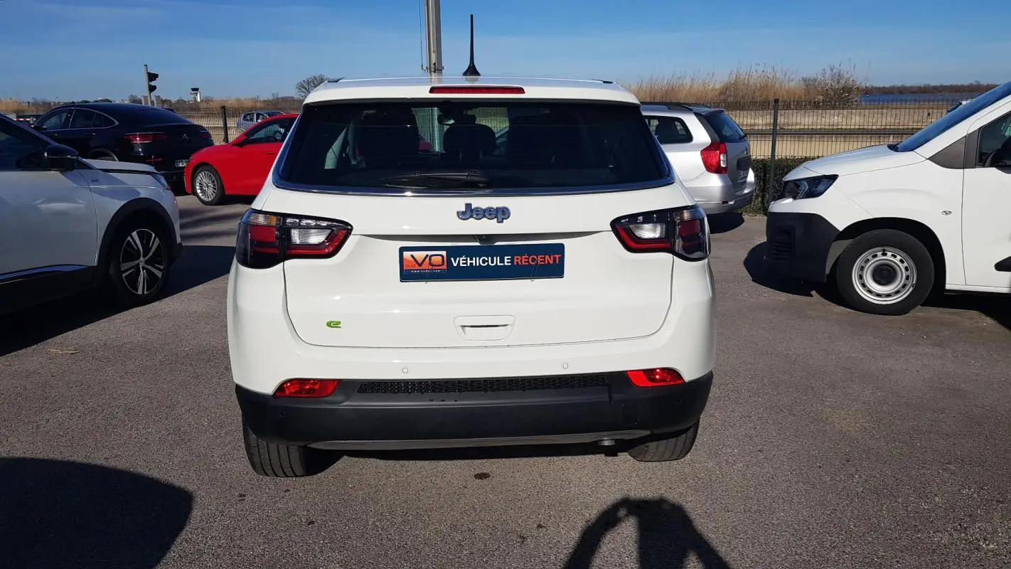 Vue arrière d'un Jeep Compass blanc 2024 avec feux LED et logo e-Hybrid sur un parking extérieur.