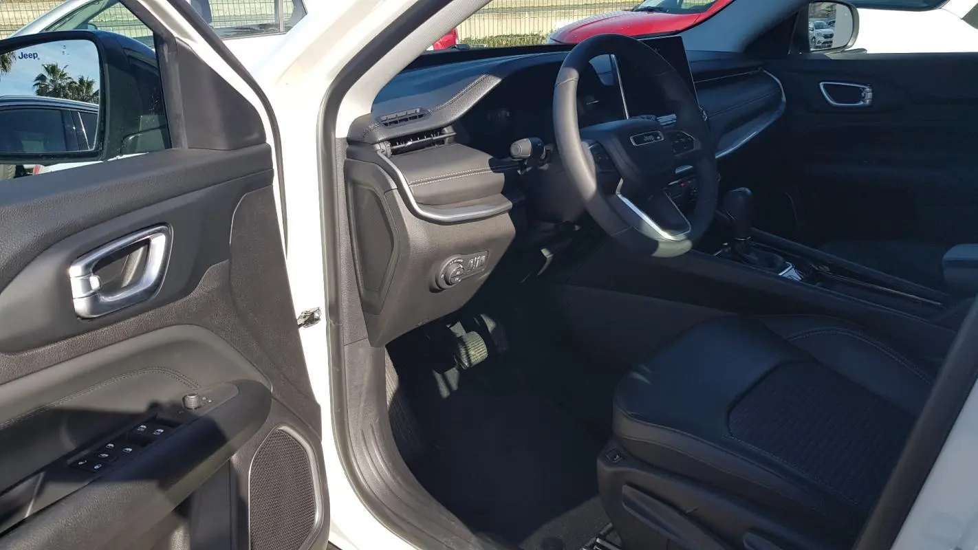 Vue intérieure côté conducteur du Jeep Compass blanc 2024, montrant le volant, tableau de bord et siège en cuir noir.