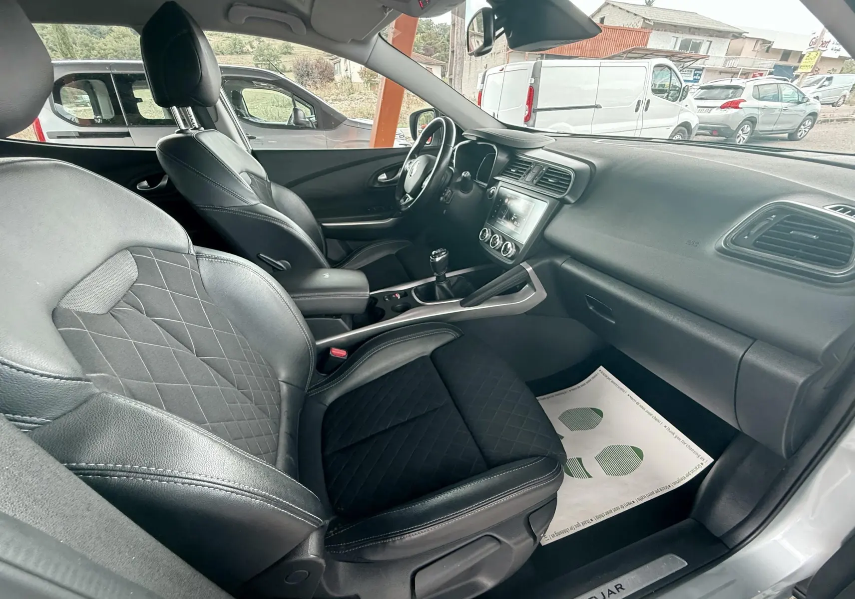Intérieur du Renault Kadjar 1,3 TCE 140CH Intens gris, vue côté passager avec sièges cuir noir et tableau de bord moderne.