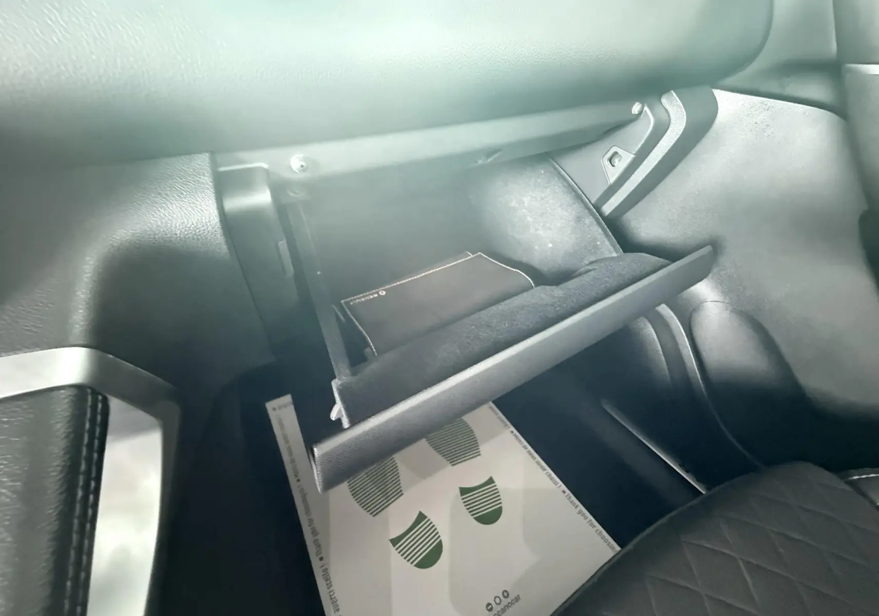 Gros plan sur la boîte à gants ouverte côté passager du Renault Kadjar gris, montrant un livret à l'intérieur.