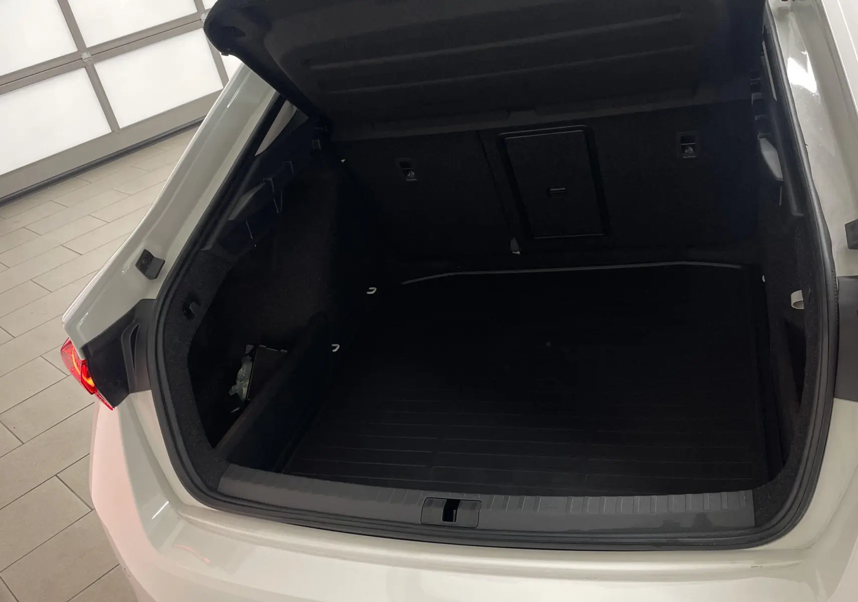 Coffre ouvert vu de l'arrière d'une Skoda Octavia blanc candy 2024 avec feu arrière droit allumé et roue de secours galette.