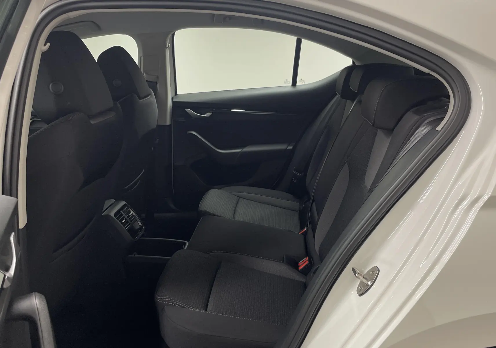 Vue intérieure côté gauche sur les sièges arrière noirs d'une Skoda Octavia 2024 blanc candy avec porte ouverte.