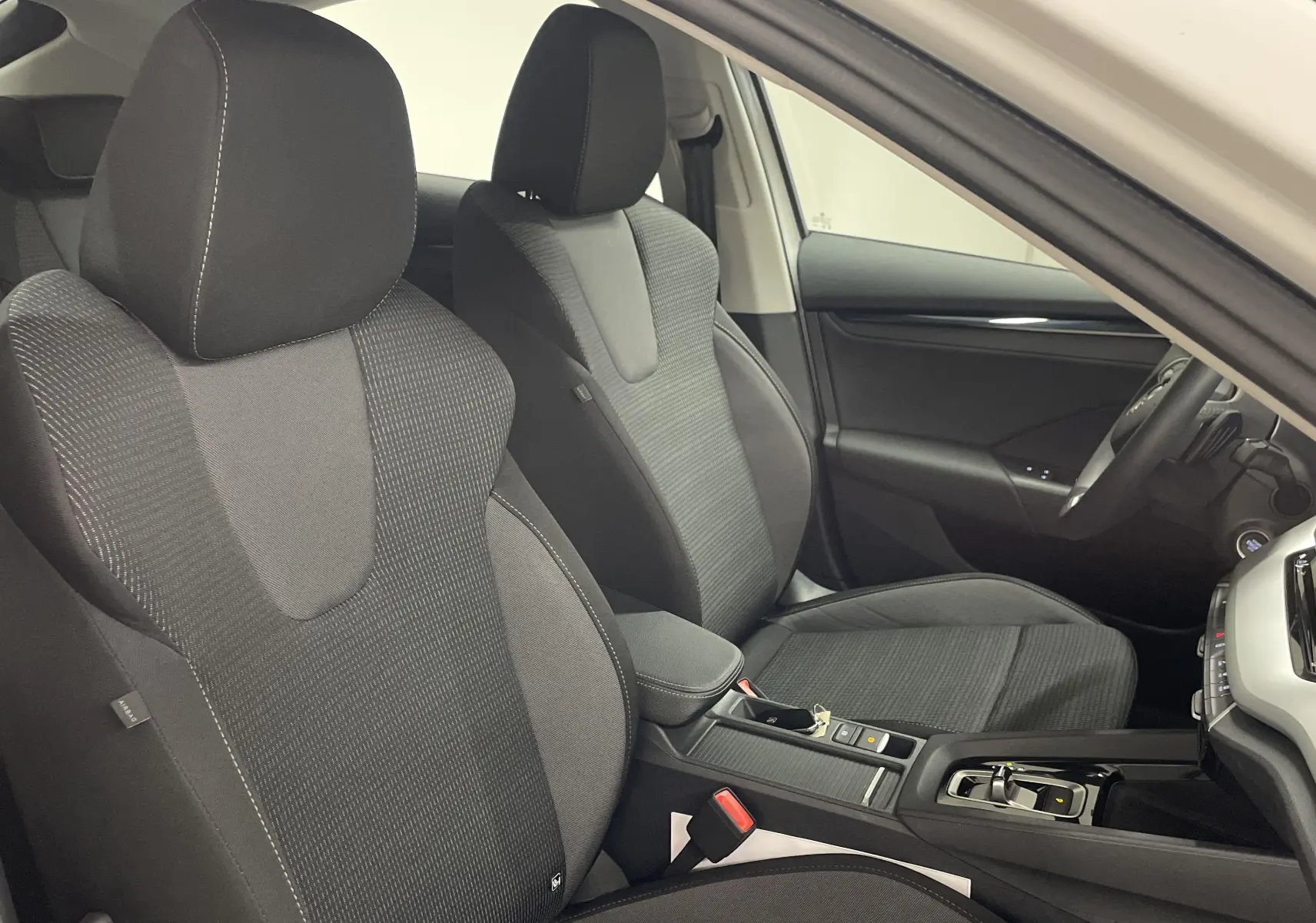 Vue intérieure côté conducteur de la Skoda Octavia 2024 blanc candy, montrant les sièges avant en tissu noir et la console centrale.
