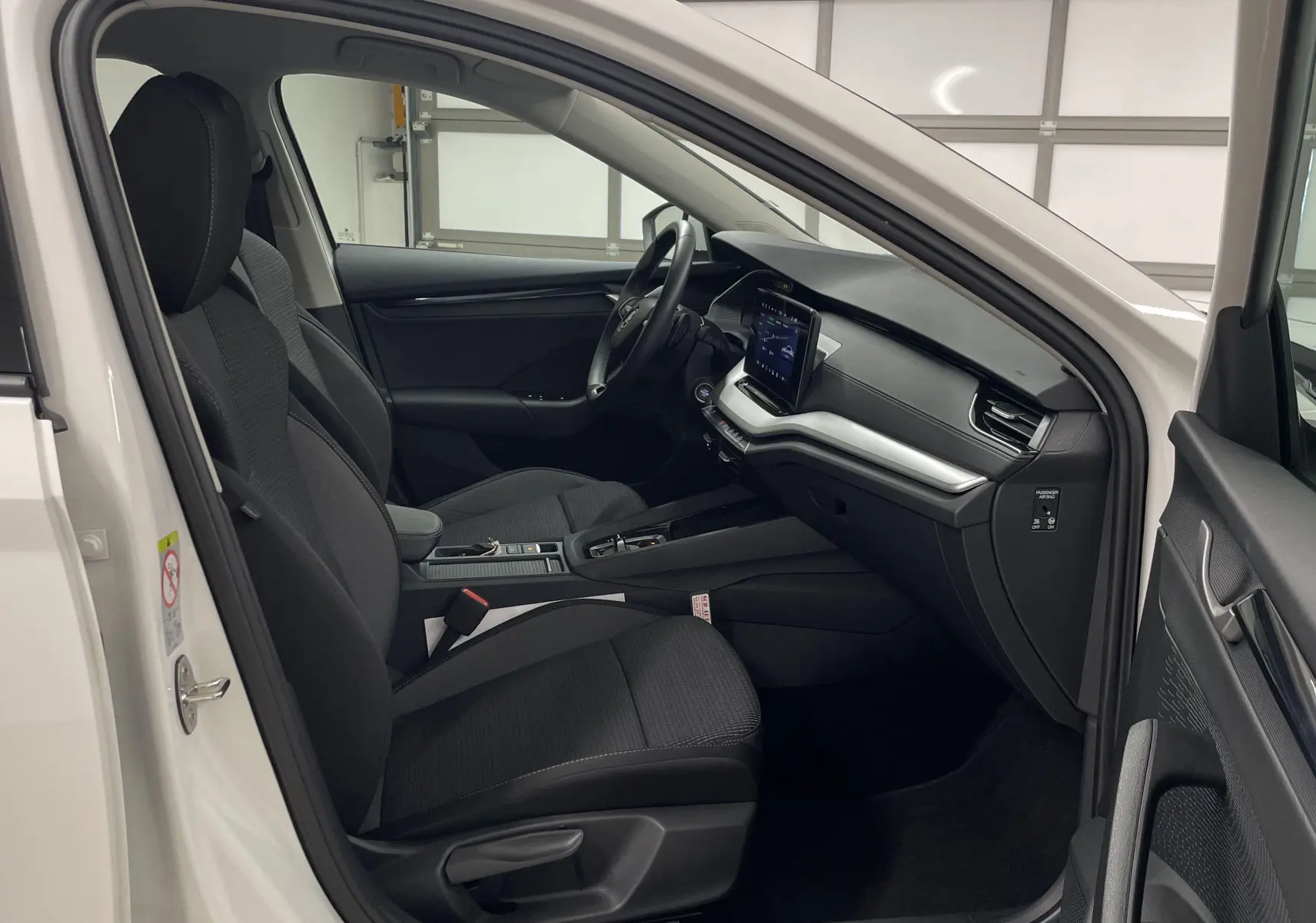Intérieur côté conducteur d'une Skoda Octavia blanche 2024, sièges noirs et tableau de bord moderne avec écran tactile.